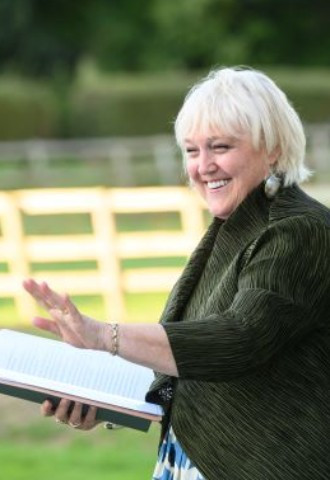 Janet in the open air, holding her hand out to guests and smiling broadly