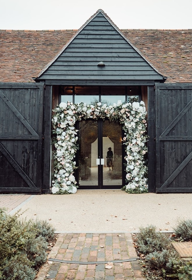 Exterior of Alfriston Gardens Barn with floral archway installation framing the entrance