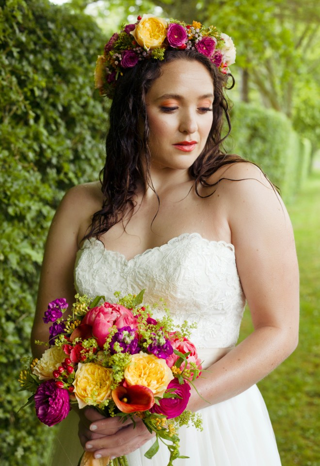 a bride holding a colourful bouquet and wearing a matching flower crown, looking stunning despite the April showers