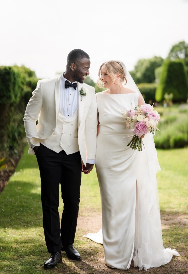 Bride and groom walking hand in hand through the gardens at Danesfield House Hotel, smiling at each other on their wedding day.