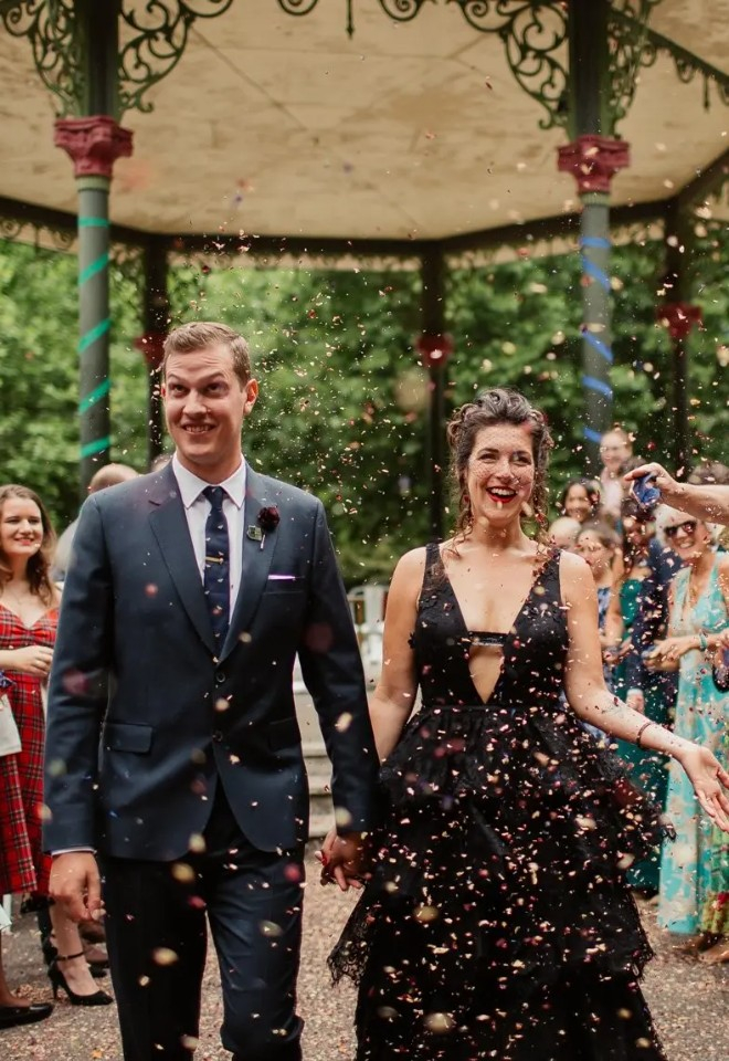 Bride and groom walking through confetti aisle on wedding day in Battersea Park. The bride is wearing a black wedding dress.
