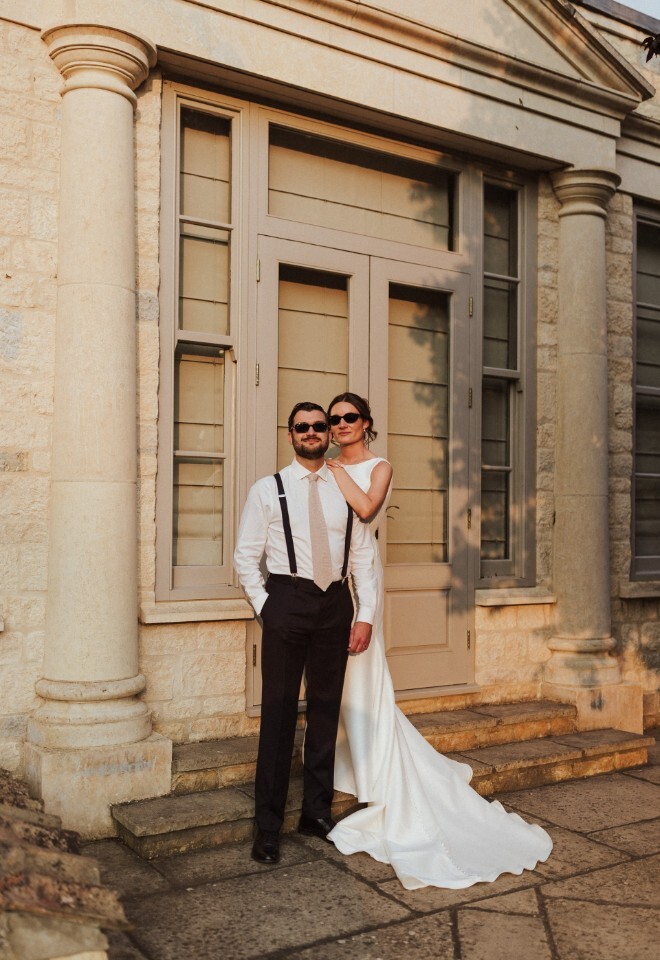 Bride and groom in sunglasses stand together outside Washingborough Hall Hotel, bathed in warm golden light against the stone façade and tall columns.