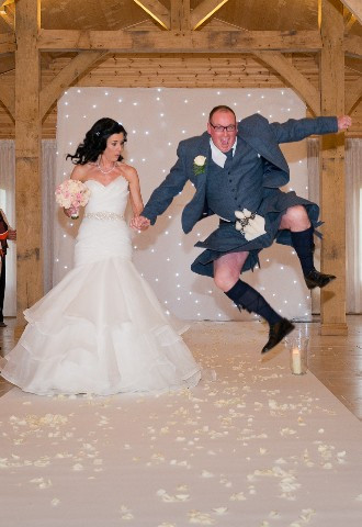 Wedding aisle walk by bride and groom in kilt jumping for joy 