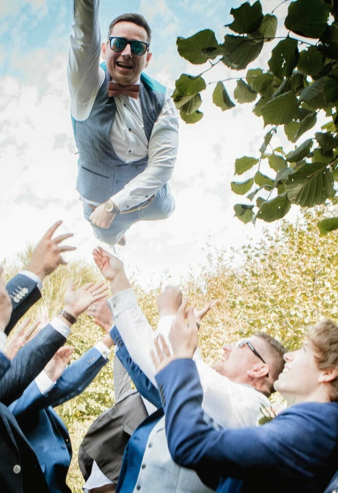 Groom tossed into the air by groomsmen at outdoor wedding celebration