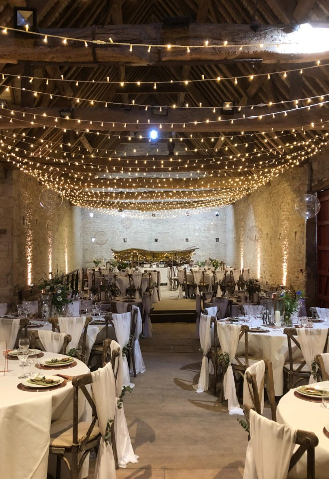 Classic round tables with oak cross back chairs and white voile tiebacks