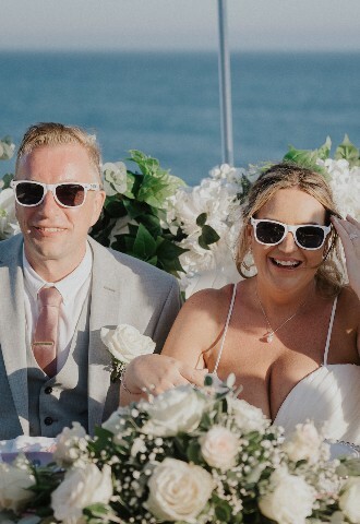 bride and groom in sunglasses sit at the top table at their wedding reception on a boat in cyprus