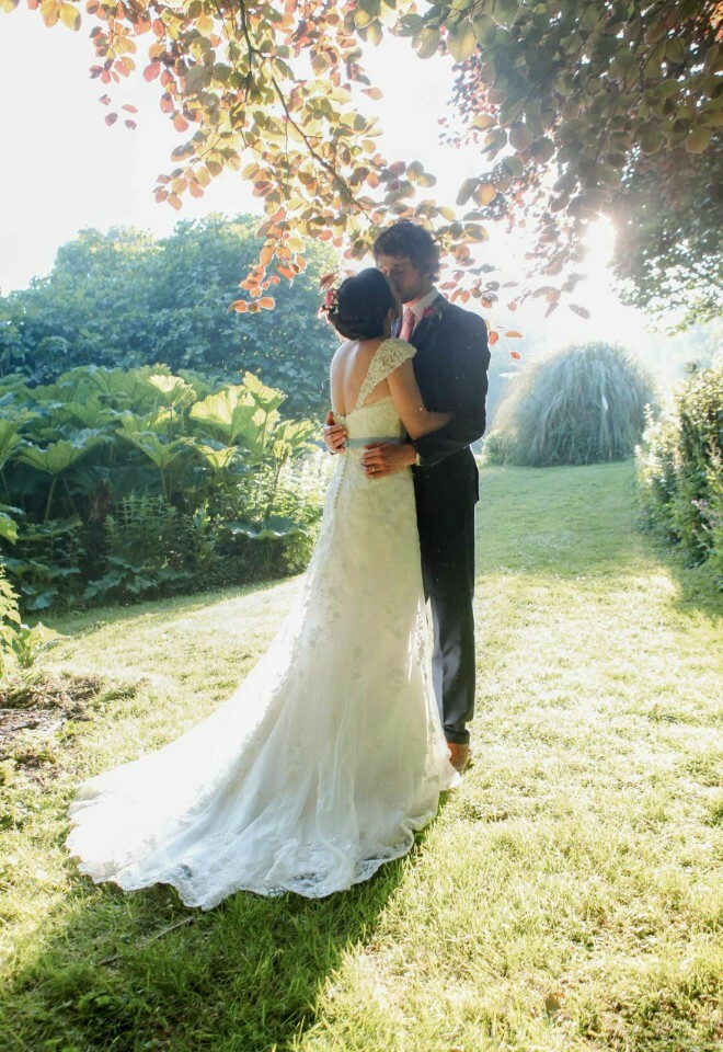 Romantic outdoor shot of newlyweds kissing under trees in evening sunlight