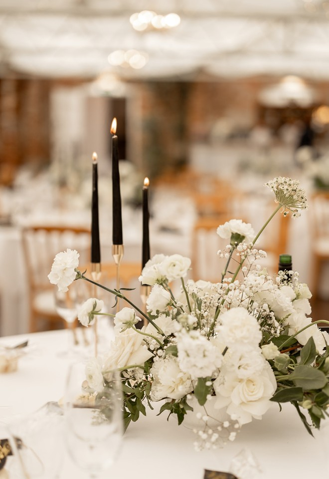 White compote bowl centrepiece of peonies, roses, allium, dianthus, eustoma, ranunculus and gypsophila with black candles at Northbrook Park