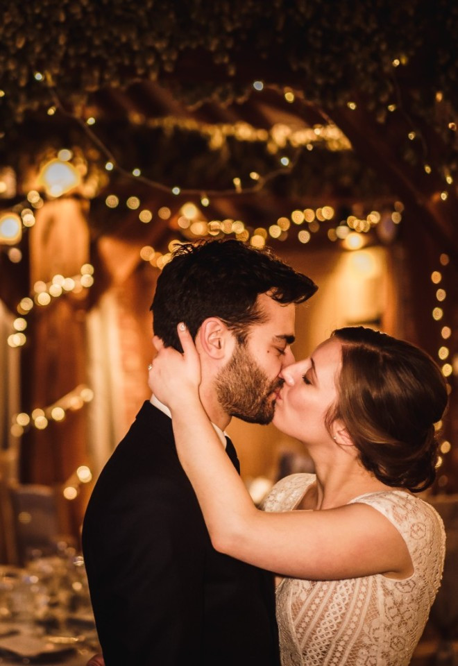 Bride and groom share a kiss in a fairylit wedding barn in Kent
