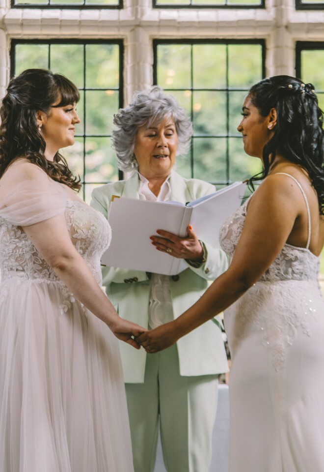 Suffolk celebrant in a green trouser suit standing between two brides as they make their I do vows