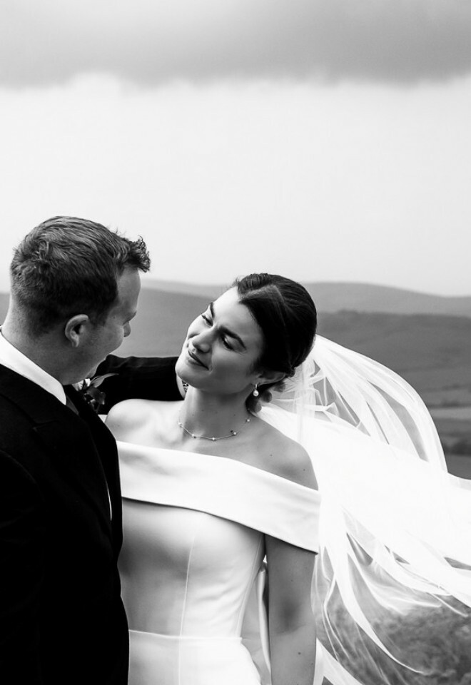 black & white image of groom & bride with her veils flowing in the wind, image by dorset wedding photographer