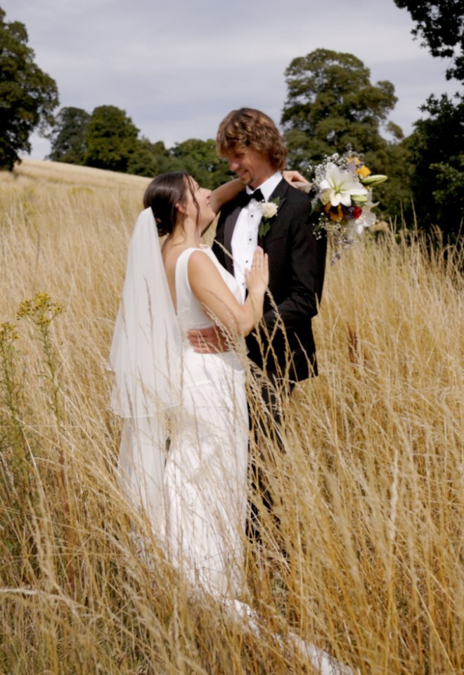 married couple in field with wedding videographer