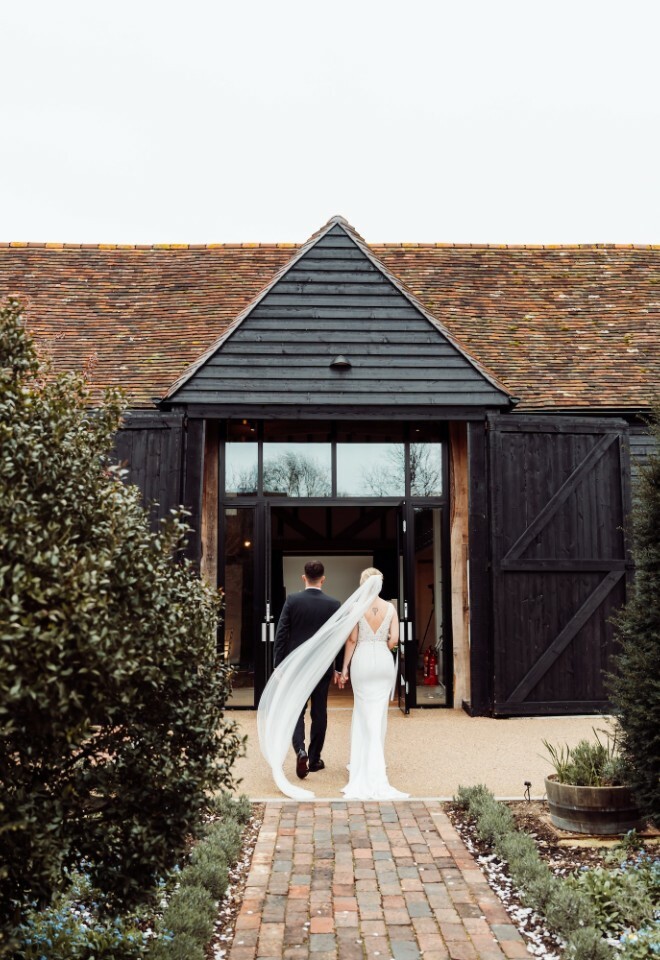 Bride and groom stand outside the wedding barn at Alfriston Gardens in East Sussex