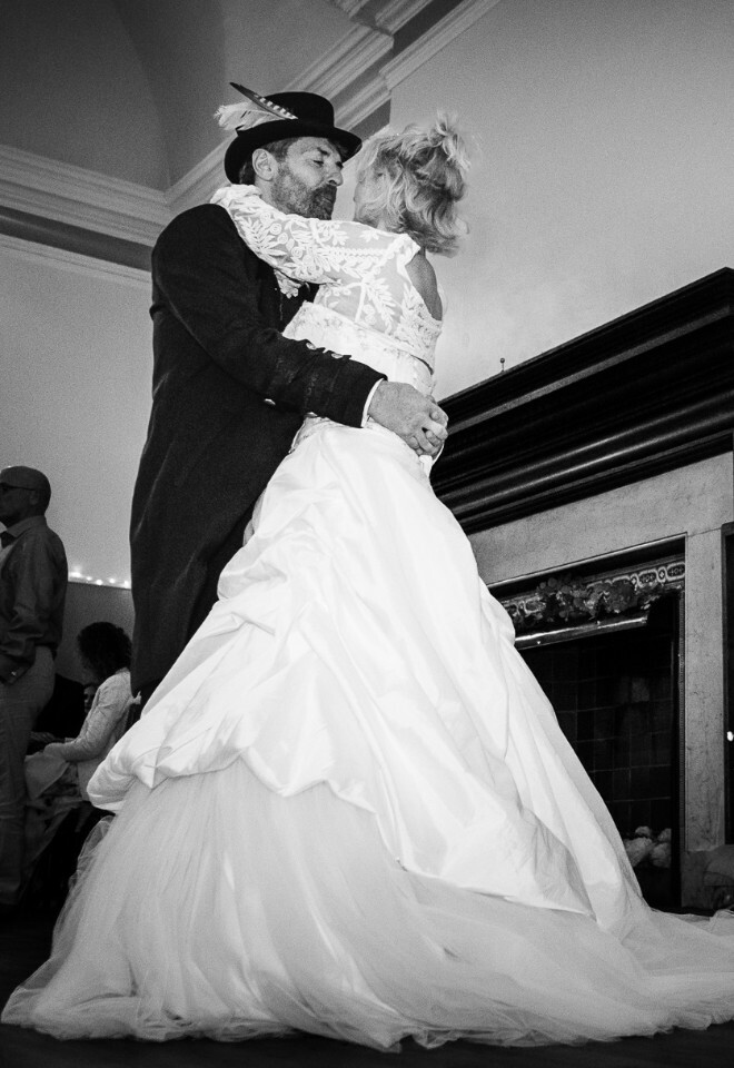 A couple shares their first dance in an elegant reception room with a grand piano in black and white photography.