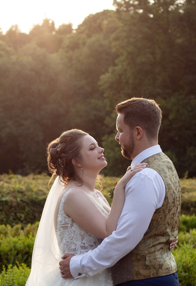 The bride and groom hold each other in the setting sunlight with the Rhinefiled house hedge maze behind them