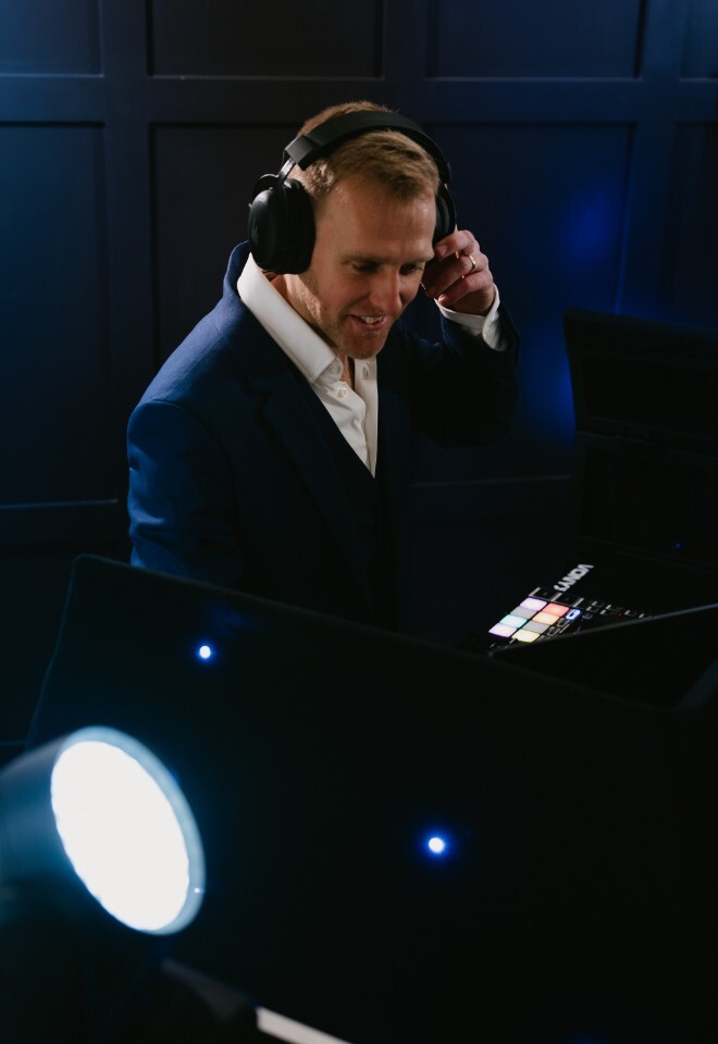 Matt Rayner, an Essex based DJ is wearing a navy suit while mixing on his controller with lighting