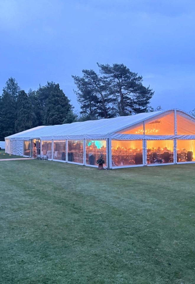 Luxury wedding marquee glowing at sunset in a picturesque countryside setting, showcasing a beautifully planned outdoor wedding reception venue.