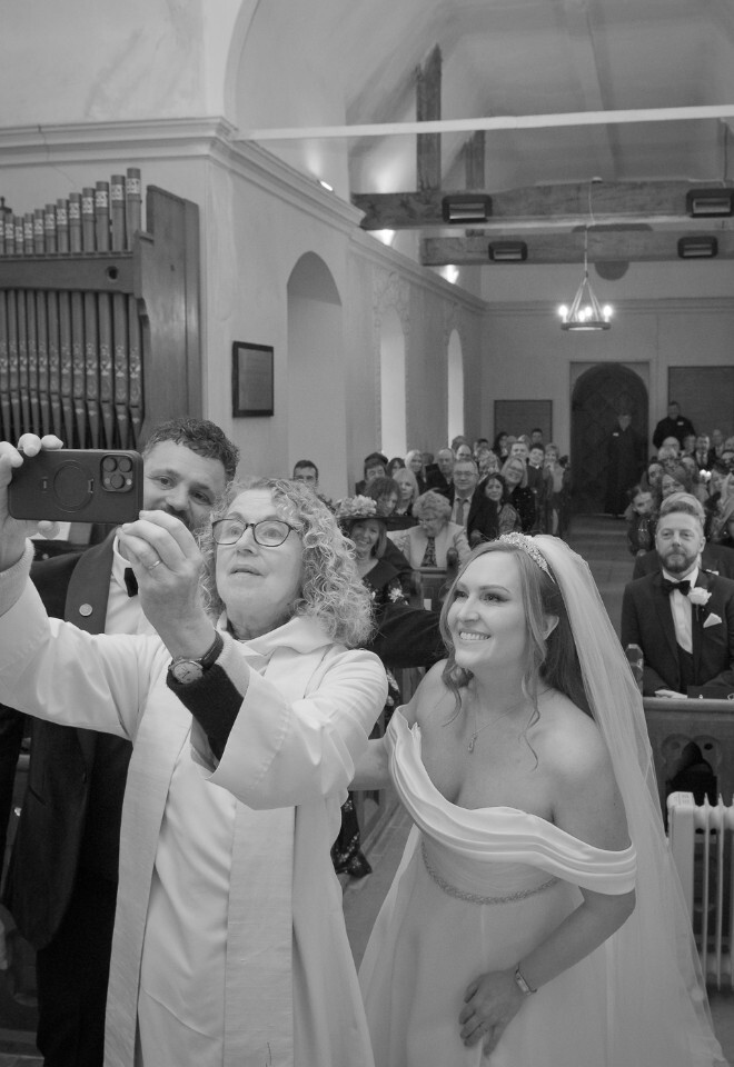 Vicar taking a selfie with bride and groom in front of congregation at Wasing Park church in Berkshire 
