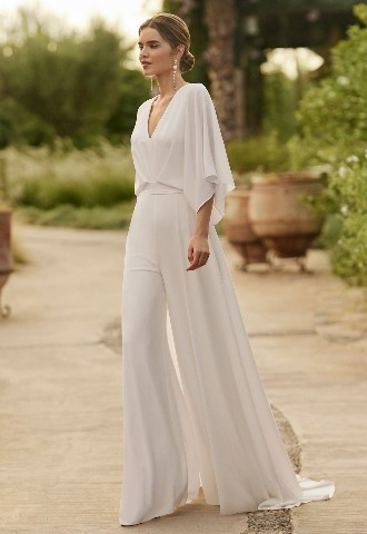 Laisa from Alma Novia - Simple and fluid bridal trouser suit/dress, crafted in crespon. With a V-neckline, V-back and a cape sleeve