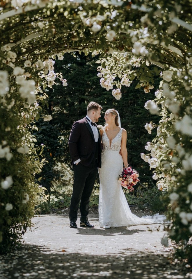 Newlyweds pose beneath rose arch on their wedding day in Kent