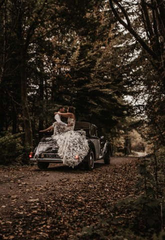 Bride and groom sat on vintage car in the grounds at Auchen Castle - a romantic castle wedding venue in Scotland