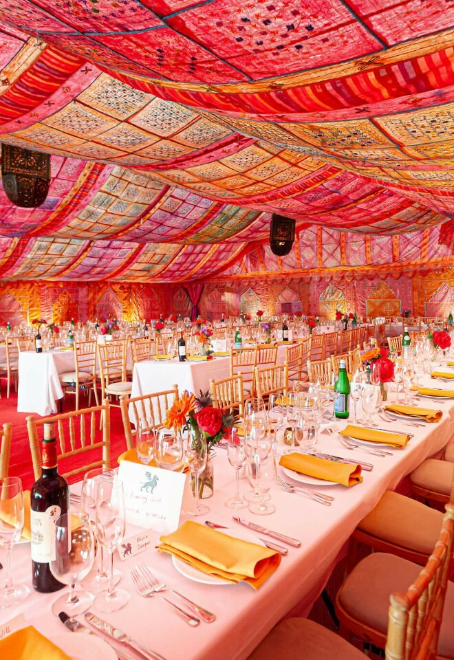 A marquee with pink and orange bombay boudoir linings and long banquet dining tables 