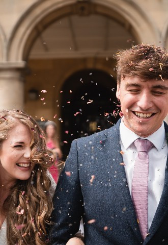 A newly married couple smiling while confetti is thrown at them