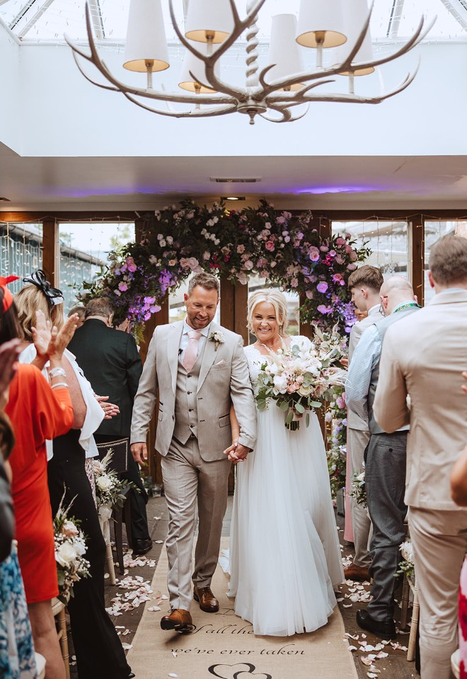 Newlyweds walking hand in hand back down the aisle following their indoor wedding ceremony at The Cock O’Barton.
