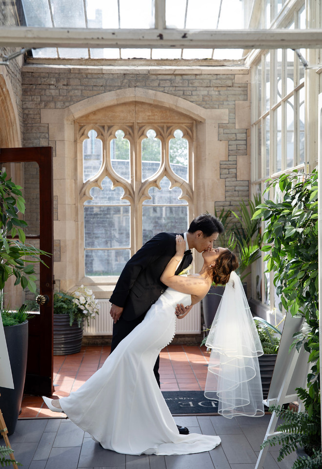 “Bride and groom sharing a dip kiss in the orangery at De Vere Tortworth Court in Bristol photographed by Katy Brothers Wedding Photography”