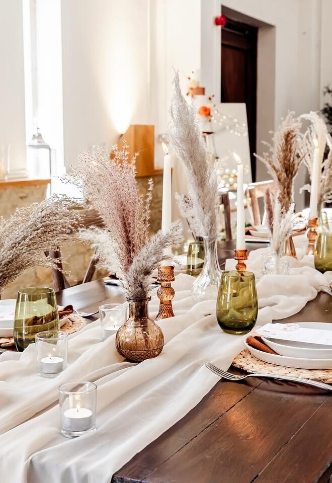 Long oak table with white runner and pampas filled vases with table settings
