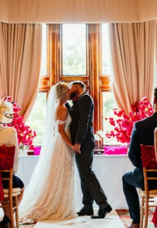 Couple kissing in the window of the Somerleyton Suite, with guests seated- Sprowston Manor Norwich