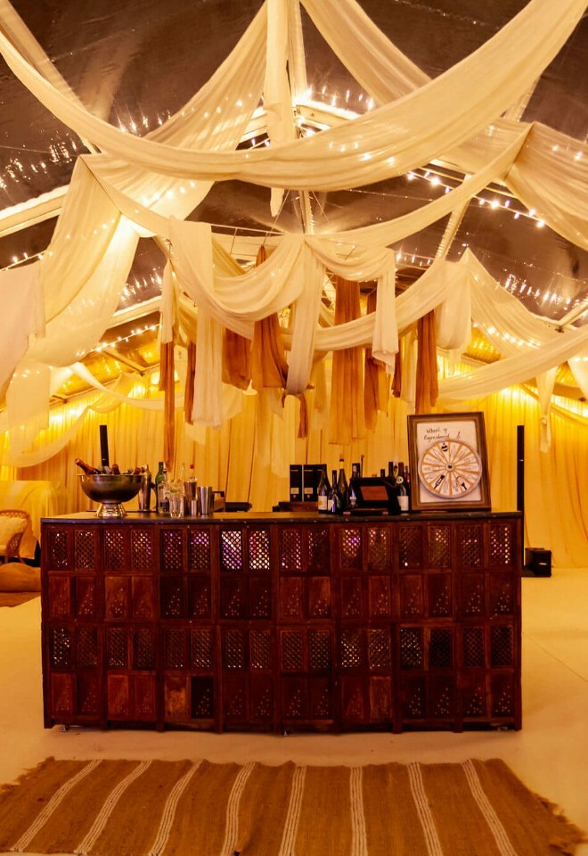 Luxury marquee with dramatic white draping with golden lighting hanging above a wooden bar