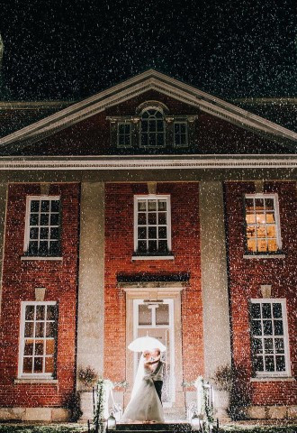 couple stood under umbrella outside manor house