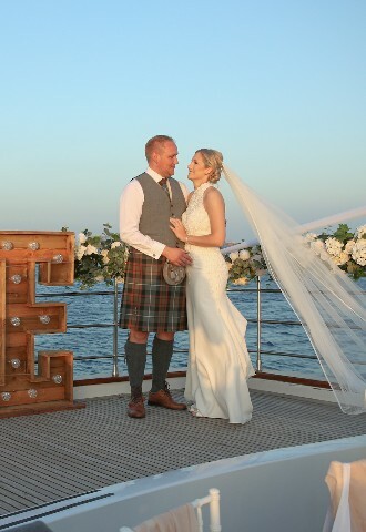 Bride and groom pose next to light up letters that spell out love, on a yacht in cyprus