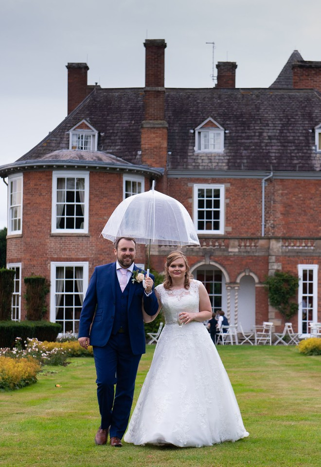 A bride and groom walk under umbrella away from the stunning Sutton Bonington Hall