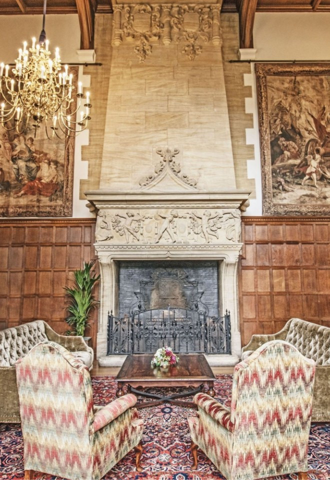 High Gallery inside North Mymms Park, featuring velvet sofas around a central fireplace, historic tapestries, wood paneling, and a brass chandelier.