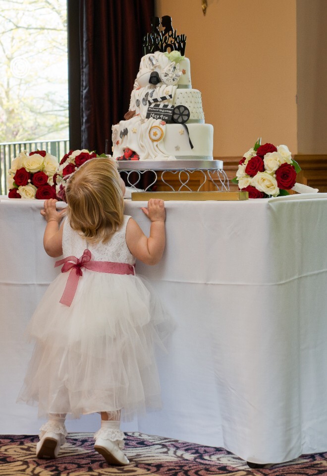 Wedding flower girl on tip toes looking at wedding cake