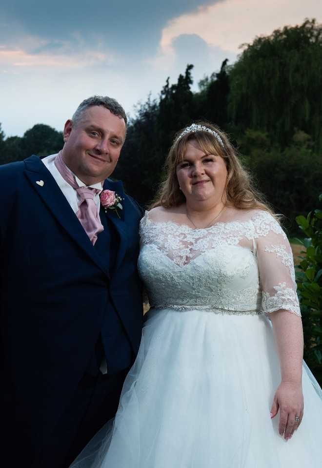 Groom and bride in the countryside at sunset on their wedding day, looking to camera