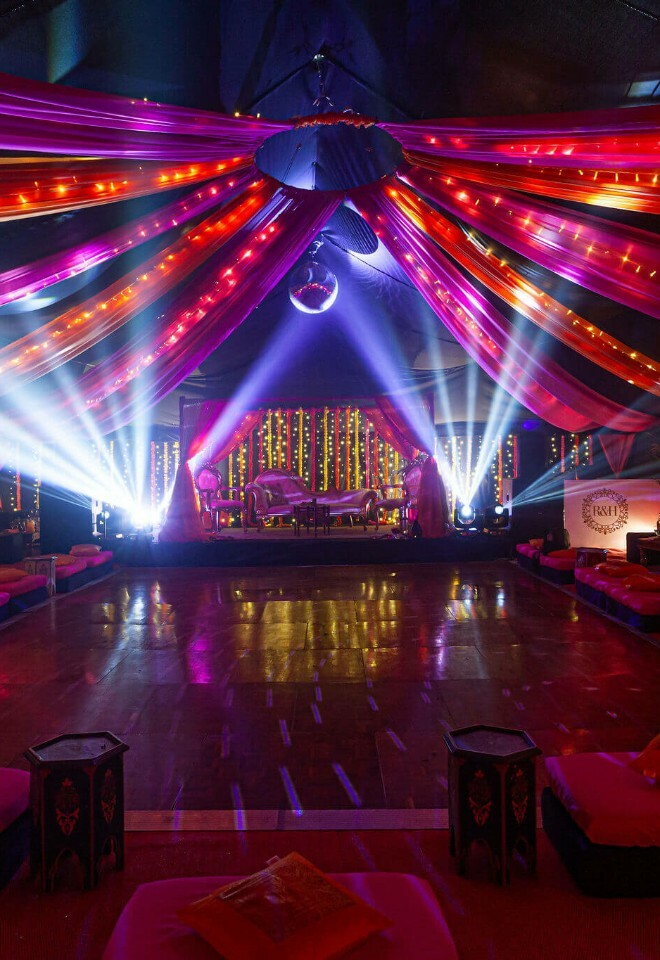 Luxury marquee for an Indian Wedding celebration with dramatic draping, uplighters and disco ball over a dancefloor surrounded by floor seating