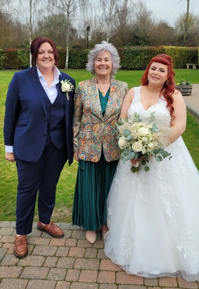 Essex wedding celebrant dressed in a green dress standing in between two brides after their wedding ceremony