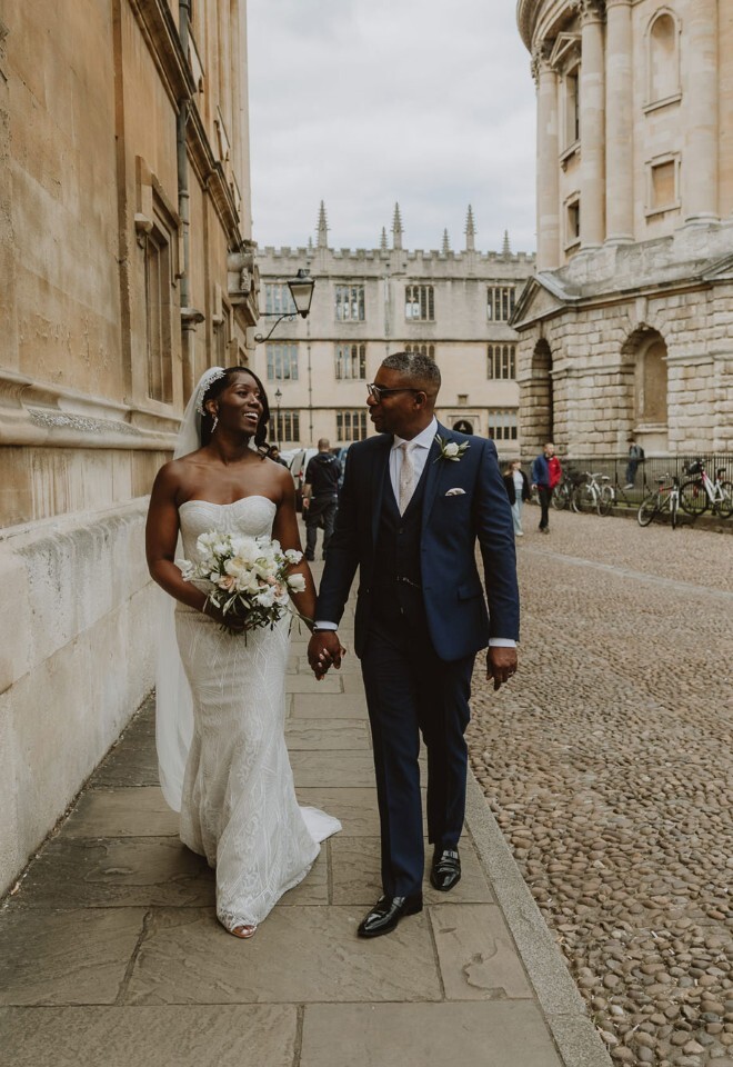 Bride and groom walking through the streets of central Oxford near the Radcliffe Camera on their wedding day, captured by V & H Photography.