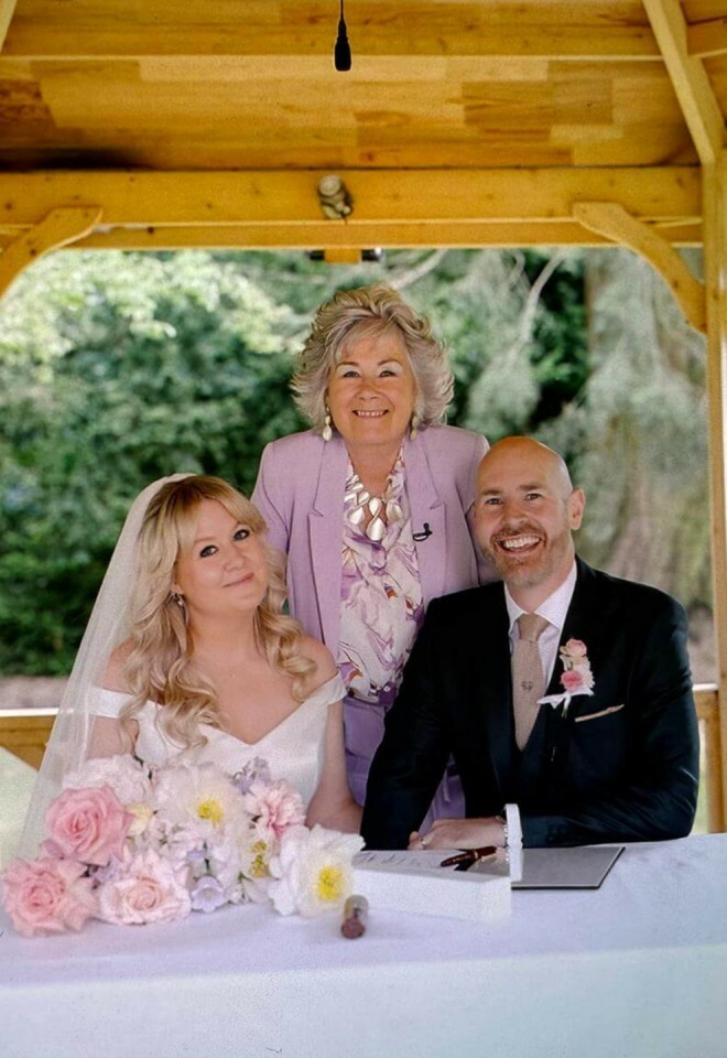 Essex wedding celebrant dressed in a lilac suit with the bride and groom signing their wedding certificate