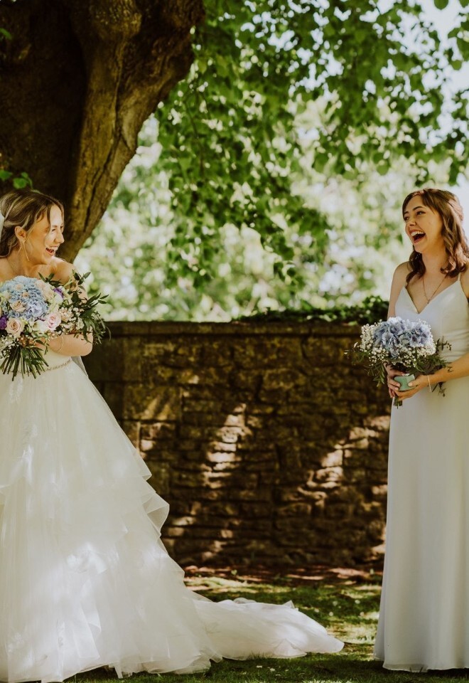 Bride holding bouquet looking back at bridesmaids with bouquets during outdoor garden wedding ceremony in Somerset by FLOWERS BY ANYA