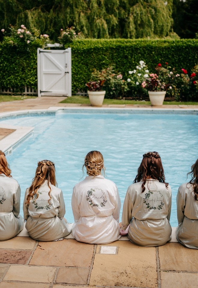 bridal party in bride and bridesmaid robes sat with legs in the pool at High House wedding venue Essex