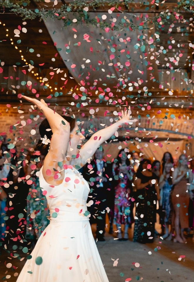 Bride and groom exulting as confetti fly in the air during their first dance, guests behind them