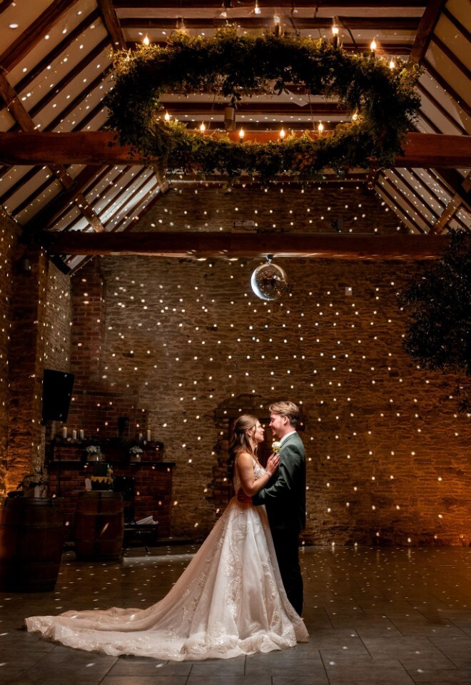 A bride and groom dancing on the dancefloor inside of one of the barns at an Oxfordshire wedding venue