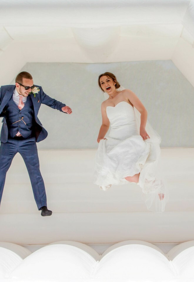 Bride and groom laughing while bouncing on wedding bouncy castle
