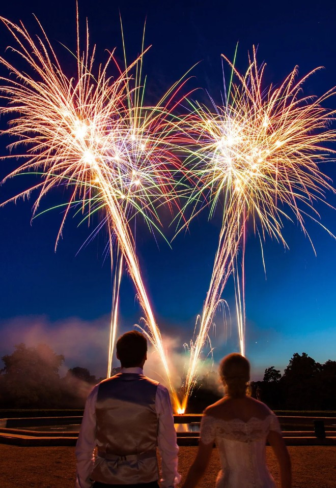 Bride and groom standing hand in hand as a professionally choreographed fireworks display by Berkshire-based Star Fireworks illuminates the evening sky