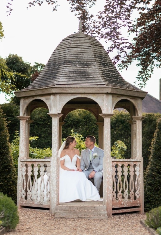 Bride and groom seated in a wooden gazebo at Washingborough Hall Hotel, surrounded by manicured gardens and topiary trees in Lincolnshire.