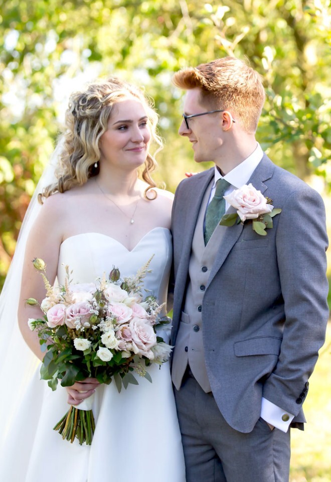 Bride and groom in smiling at each other in front of apple trees